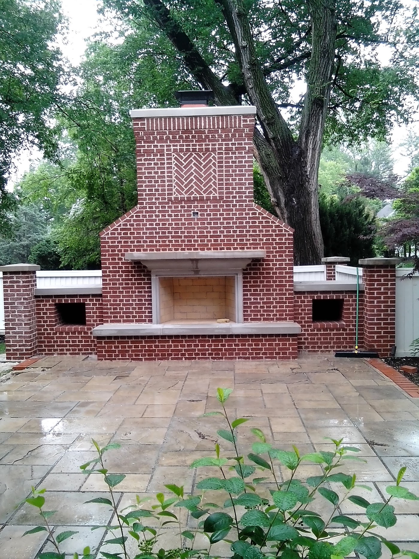 A brick outdoor fireplace with a herringbone panel and stone hearth, built by Meyer Masonry